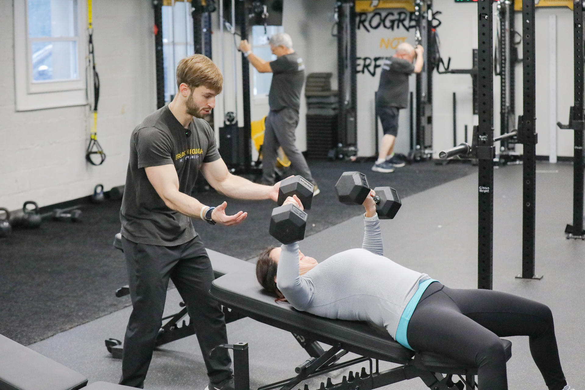 Coach helping a member with dumbbell bench press form at Breakthrough Performance